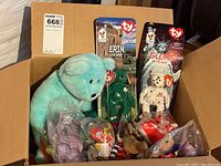 Box containing multiple Ty Beanie Babies plush and packaging, including loose and packaged bears.