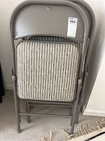 Back view of four folded metal chairs with padded woven fabric seats, stacked together.