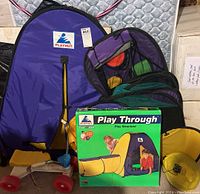 Photo showing Playhut Play Through play tent with tunnel and purple storage bag, box with product image and two kids playing, toy vehicle seen to the side.