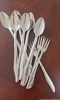 Eight vintage stainless steel spoons and forks with simple linear design laid on table.