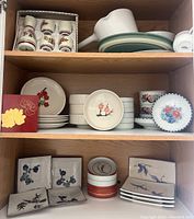 Three shelves of vintage Japanese ceramic dishes and tableware including pouring vessel, cups, bowls and decorative plates.