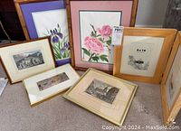 Lot of six framed art pieces including floral and architectural prints, arranged on floor leaning against a wall.