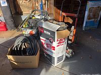 Photo showing Toro Ultra blower box, coiled garden hose, wheelbarrow frame, gloves and rake in garage setting