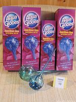 Four Aqua Globes hand-blown glass watering bulbs in original packaging, three large and one small, all blue with individual patterns.