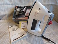 Photo showing the iron next to original box and owner's manual, displaying model details and appearance.