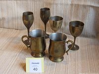 Photo of two pairs of brass goblets and two smaller brass handled cups on a striped fabric background