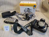 Display of the three cameras: Kodak EasyShare Z740 with box, Canon SureShot 85 Zoom with case, and Canon EOS A2E camera with strap.
