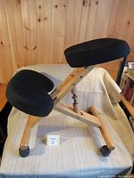 Side view of ergonomic kneeling chair showing wooden frame, black padded seat and knee supports, sitting on four locking caster wheels.