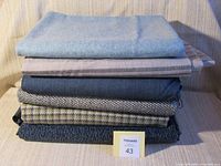 Stack of seven different fabric pieces showing variety in colors and textures including solid, striped, and patterned textiles.