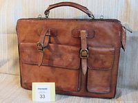 Front view of Giudi Collection leather bag showing two front pockets with buckle straps and handle.