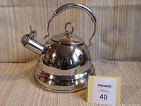 Front angled view of the polished stainless steel tea kettle showing spout with hinged cap and top handle.