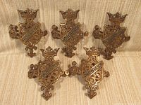 Five identical curved brass escutcheons with ornate heraldic design arranged on fabric background.