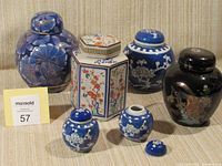Photo shows six oriental ginger jars arranged in two rows with various shapes and sizes, predominantly blue with floral and geometric patterns, including one black jar with painted scene.