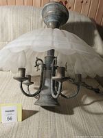 Photo showing the lamp with scalloped opaque white glass shade, central light, and five candle bulb holders on curved metal arms.