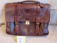 Front view of the brown leather Roots briefcase with two adjustable latched straps and central lock.