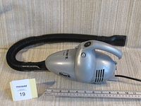 Side view of silver Shark Euro-Pro X handheld vacuum cleaner with black detachable hose coiled around it on a beige fabric surface.