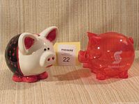 Painted ceramic piggy bank and red plastic piggy bank side by side