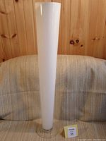 Full view of the tall, slender white glass vase placed against a wooden background and fabric surface.