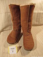 Front view of pair of tall brown suede FitFlop boots on couch with numbered card in front.