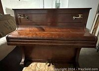 Front view of the antique upright piano showing dark wood finish and brass candle holders on the front panel.