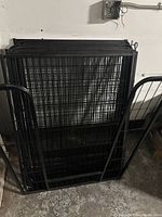 Stack of black metal animal fencing panels, showing front and side views.