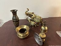 All brass items together on table: two Indian-themed brass vases, two elephant figurines, brass mini spittoon, brass oil can, and miner's carbide lamp