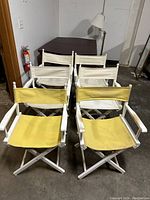 Six folding director's chairs shown in group with four white fabric chairs behind two yellow fabric chairs.