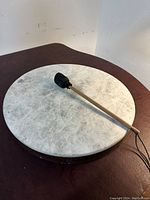 Top view of the round hand drum showing natural drum skin with some spots and included wooden mallet with black padded head lying on the drum.