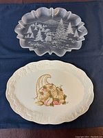 Both platters shown on dark blue fabric, glass Christmas platter on top, ceramic cornucopia platter below