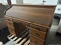 Front view of wooden roll-top desk showing closed lid and drawers with missing pulls on the left.