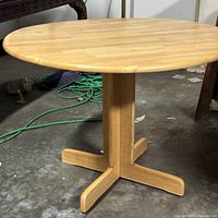 Full view of the round light oak table showing the drop-leaf sides and base structure.