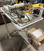 Tile saw on metal stand with basin tray and motor housing, cables and adjustable platform visible