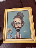 Front view of framed clown print depicting a sad clown holding a flower, in light wood frame with gold accents.