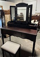Front view of vanity with folding mirror and padded stool in a room with other furniture.