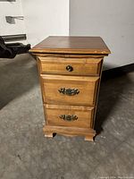 Front view of the wood nightstand showing the three drawers and metal pulls, minor scratches visible on surface.