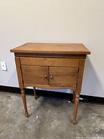 Front view of pedestal cabinet showing light wood finish, two cabinet doors, and four turned legs.