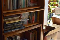 View of three shelves packed with books of various genres and sizes including thick atlases and novels.