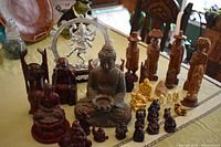 Wide view of collection of over two dozen Buddha and Hindu deity figures, various sizes and materials, with some traveler figurines in the back and a frog placed on the largest Buddha.