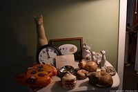 Wide shot showing all cat figurines, clock, trinket box, small wax figurine, and framed cat artwork arranged on a surface under warm lighting.