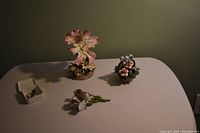 Three porcelain floral figurines arranged on a flat surface, including a small boxed pin