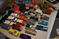 Over two dozen assorted metal toy cars and trucks in various colors including red, yellow, silver, black, blue, and orange displayed on a table