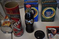 Photo showing Coca-Cola Dale Earnhardt bottle in collector container, unopened popcorn can, and Lord of the Rings glass goblets boxed