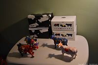 Photo showing all three figurines with their original packaging in the background. The figurines depict cows with colorful and artistic designs.