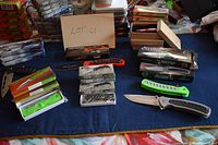 Photo of 18 new cutlery tools with visible packaging. Variety of folding knives and cutter tools in colors orange, green, black and brown. Three Victorinox with visible pre-printed logos.