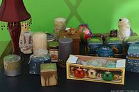 Candles, candle holders, ceramic animal-shaped holders, and boxed small colored candle holders displayed on a surface with a green background.
