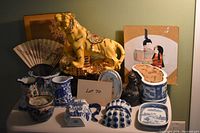 Porcelain tiger figurine surrounded by assorted blue and white porcelain pitchers, planters, and small porcelain pieces, including decorative fan and small pictures