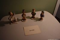 Four Hummel figurines shown from the front in natural light with paper label Lot 87 visible.