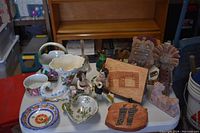 Wide view of all items showing porcelain, pottery, figurines, sculptures, jug, and bell