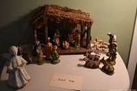 Full set of nativity porcelain figurines with stable and plastic sheep, displayed on table with neutral wall background