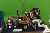 Wide view of assorted Latin American folk art items displayed against a green background, showing the variety and number of collectible objects.